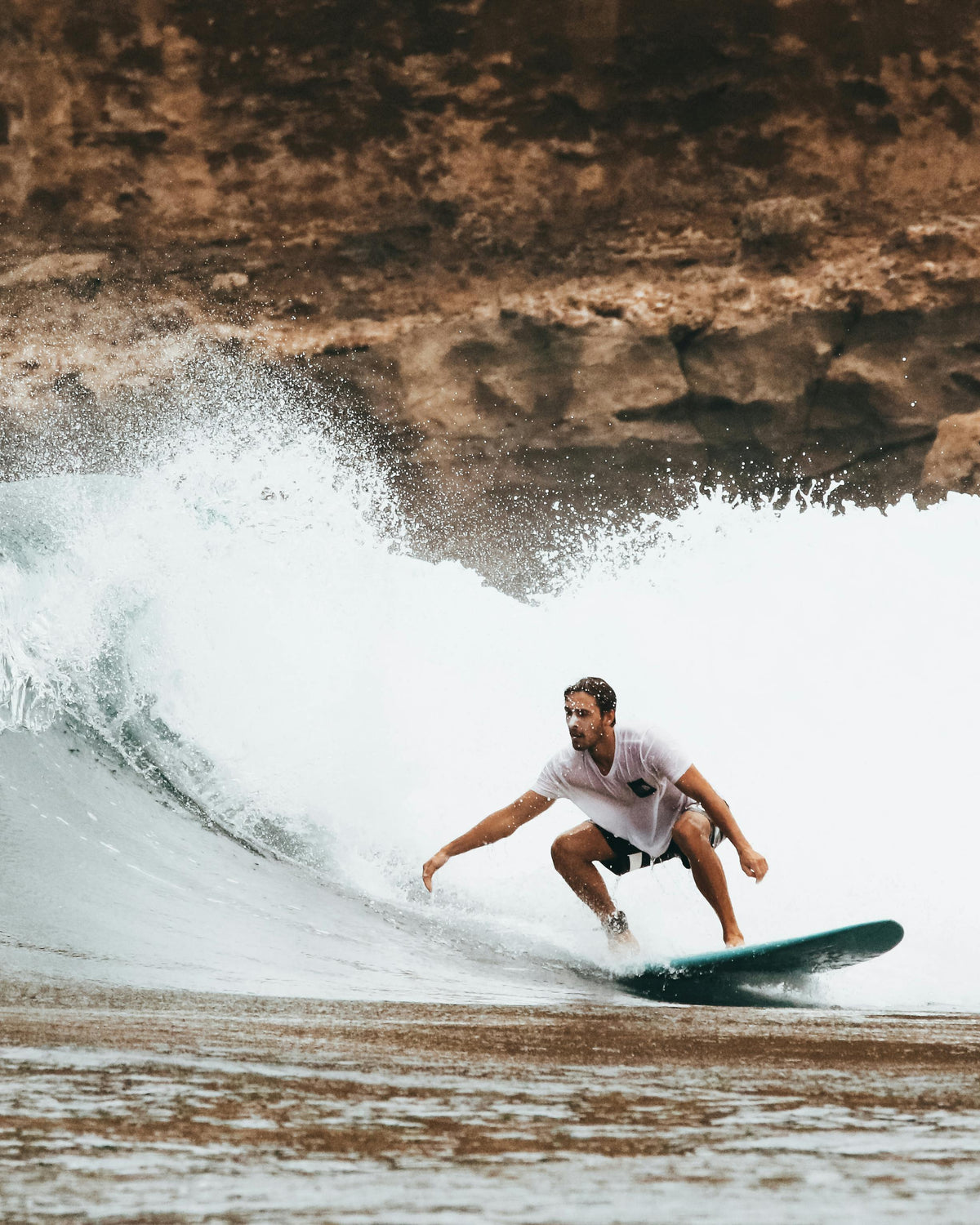 Surfer riding a wave beside a rocky coastline